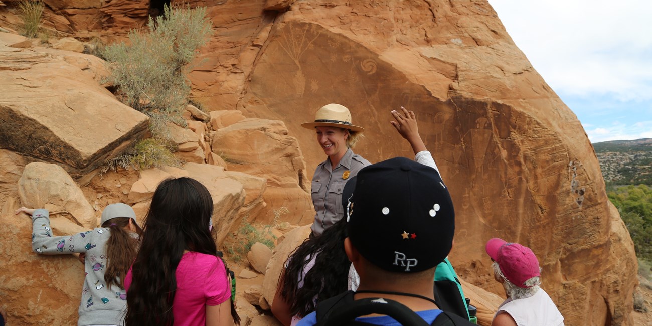 A ranger presents a program to a group of visitors in front of a petroglyph site.