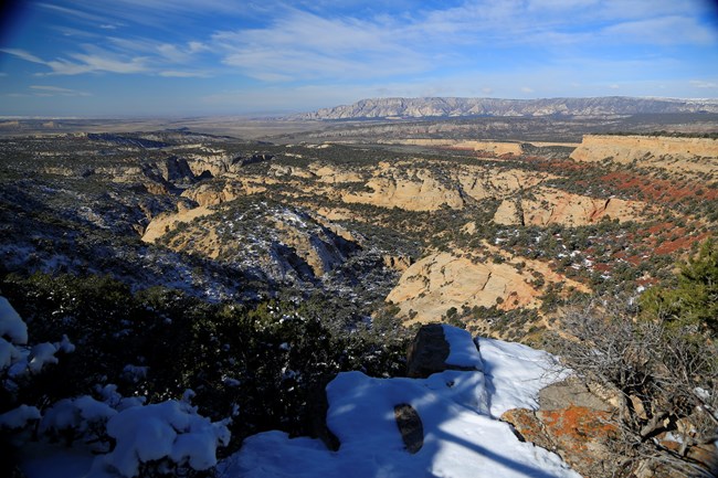 A view of colorful rock layers in an arid landscape, dotted in places with snow.