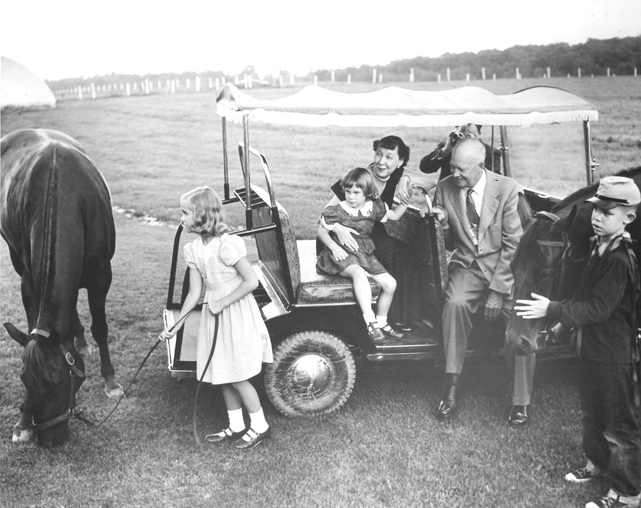 Black and white image of the Eisenhowers on a golf cart with their grandchildren