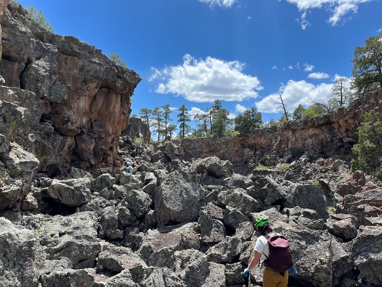 Two people wearing helmets are scrambling on large rocks in a collapse trench.