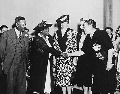 Two women shake hands as others look on.