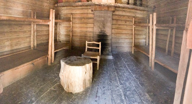 Un cuarto de madera on cuatro literas, un lugar para fuegos y un tacón en el medio del cuarto.