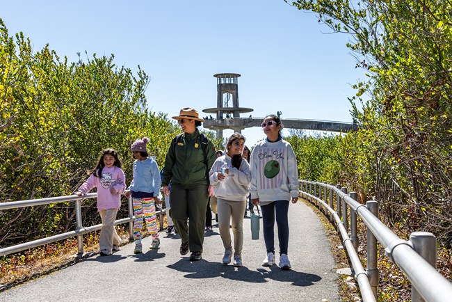 A ranger walks with students on a trail in front of a large cement tower