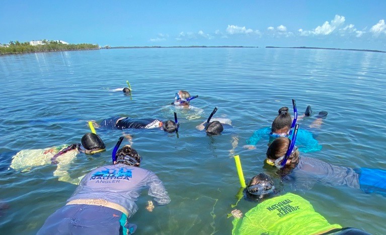 Students and an adult snorkeling facedown in blue waters