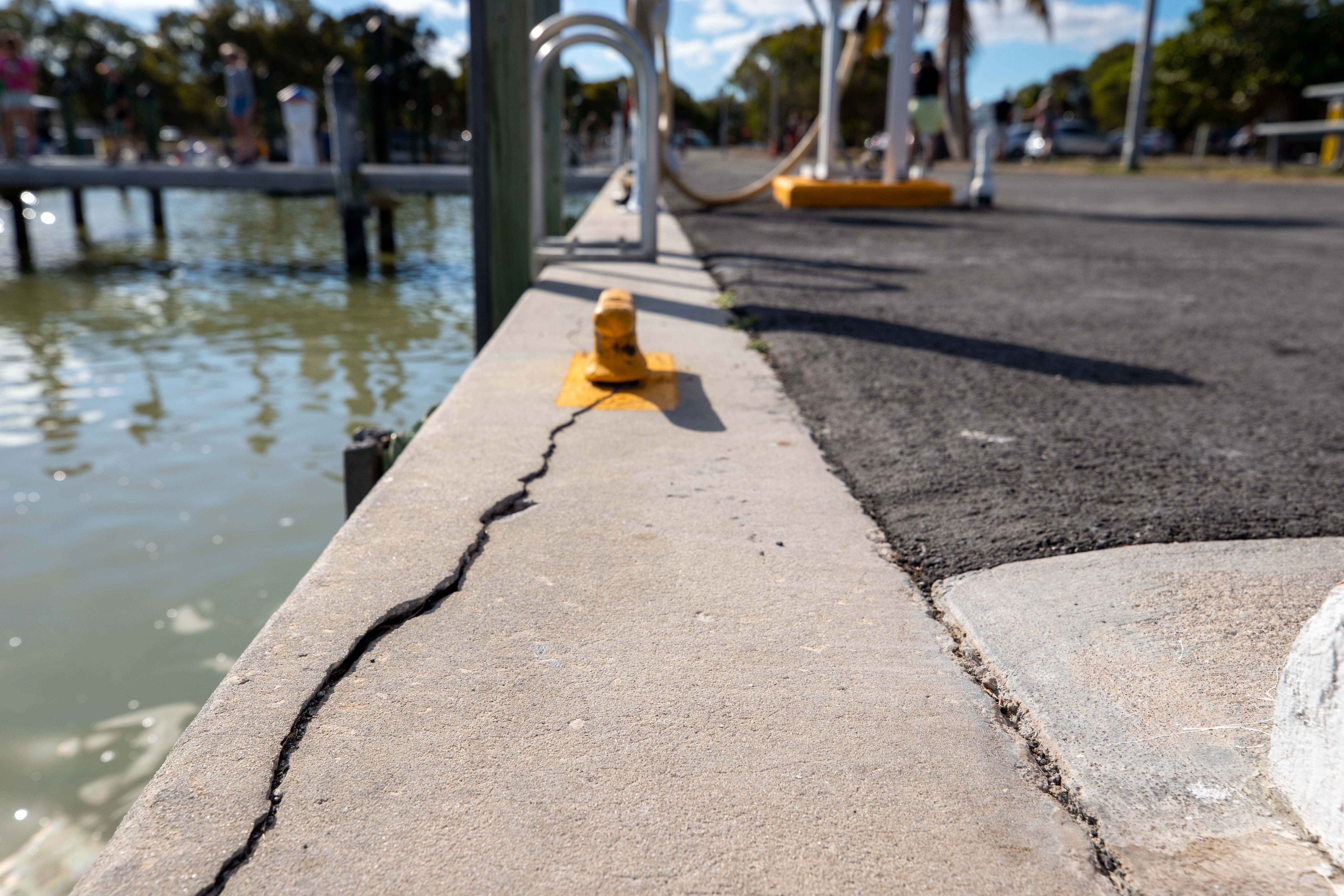 A long crack in a cement seawall runs up alongside the murky water in the marina.