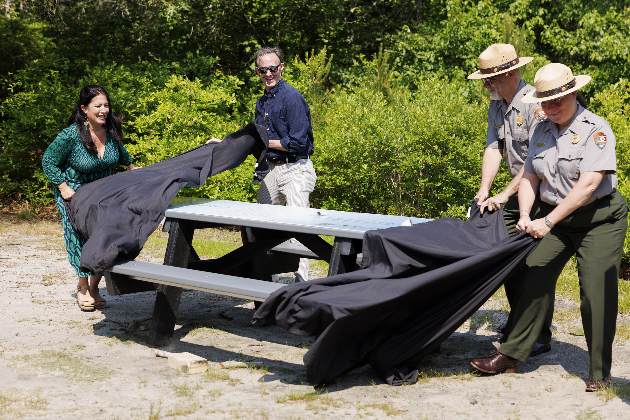 Four individuals remove black table cloths from an outdoor picnic table