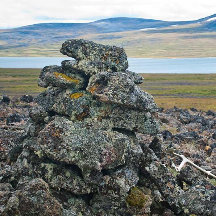 A lichen covered rock carin stands before a large lake.