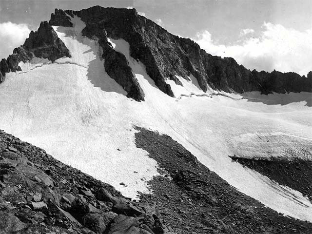 The black and white circa 1900 photo shows a dark mountainside that is half-covered by a white glacier. As the handle moves to the right, the photo transitions to a color 2004 photo of the mountainside where only a quarter of it is covered by glacier. Next is another 2008 color photo with the glacier shrinking even more.