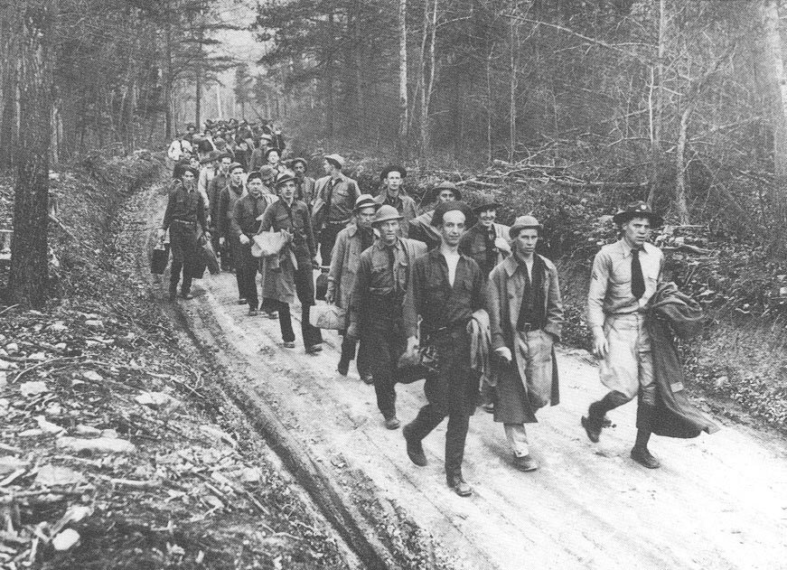 A column of young men walking down a dirk road.