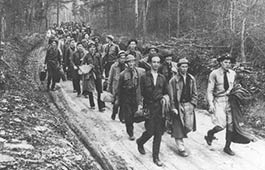 A column of young men walking down a dirt road.