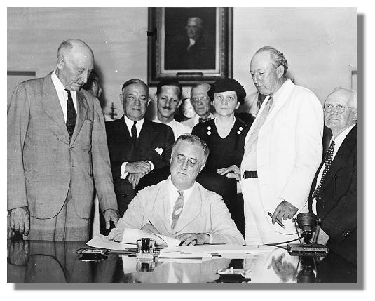 FDR signing the Social Security Act at his desk with others in the background.