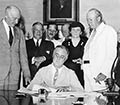 FDR signing the Social Security Act at his desk with others in the background.
