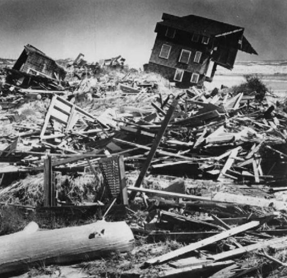 A black and white photo of wrecked homes against a ocean backdrop.