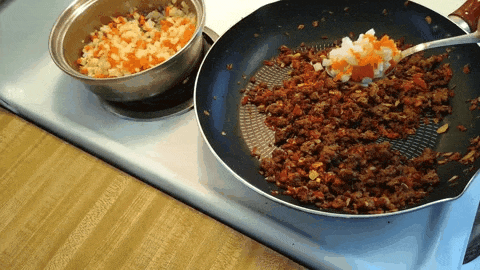 Moving image showing a skillet next to a pot of drained chopped potatoes and carrots being added to the skillet of sautéed onions, tomatoes, seasoned ground beef, chopped almonds and whole raisins being combined together.