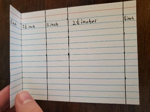 An index card is creased along a black line dividing measured sections.