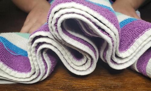 Layers of a folded towel fold over each other as two hands push the ends of the towel together.