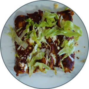 On a white plate, four enchiladas in red chile sauce are topped with lettuce and cheese.