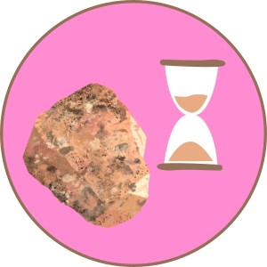 A chunk of the pink coarse pikes peak granite it shown beside an hourglass with pink sand.