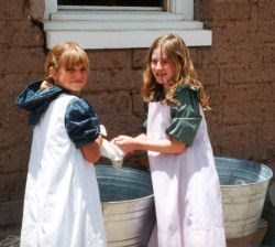 A couple of young girls in living history apparel washing clothes in front  of the restored kitchen.