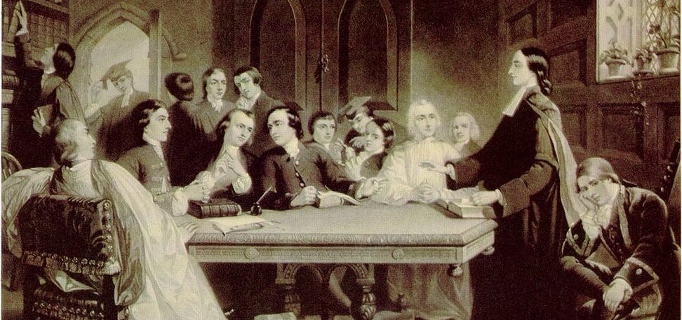 Group of men around table. One man preaching with open book in front of him.