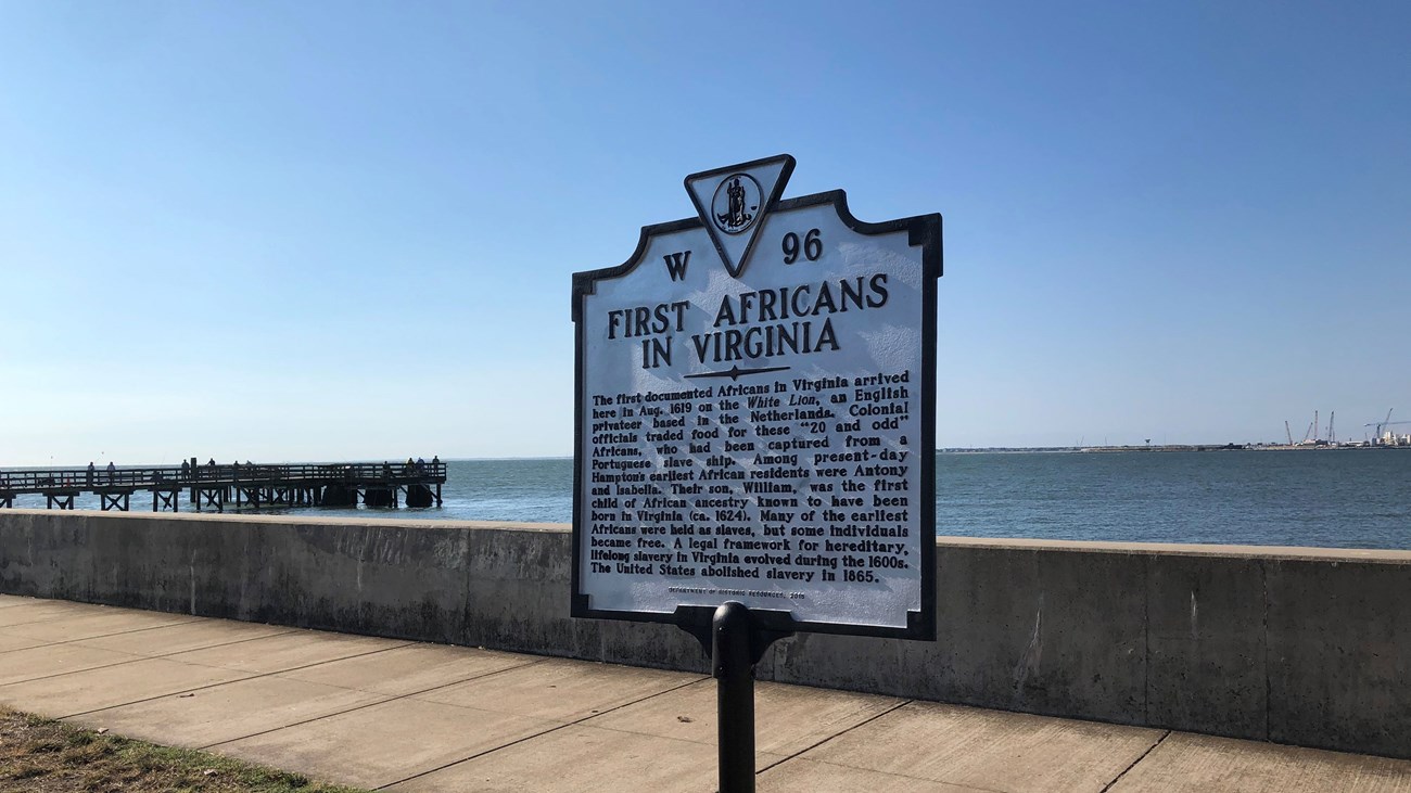 A historical marker sign on a seawall notes the arrival of the first Africans in Virginia.