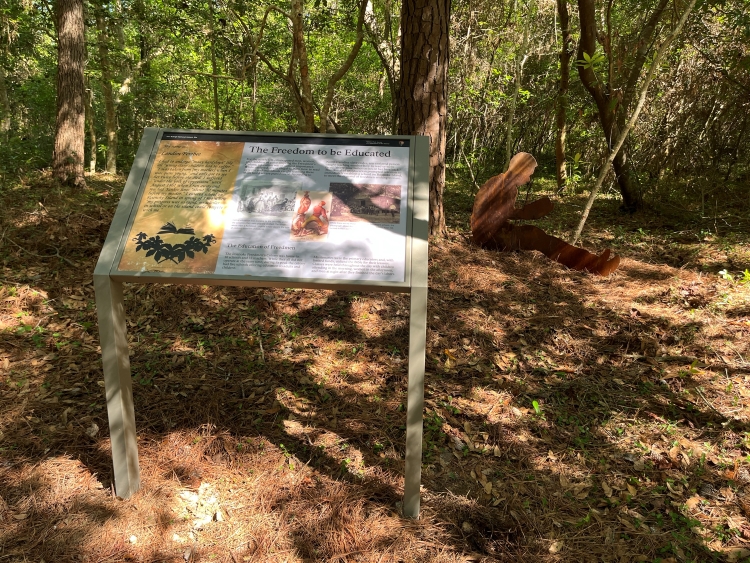 Photo of an educational panel and silhouette along wooded trail.