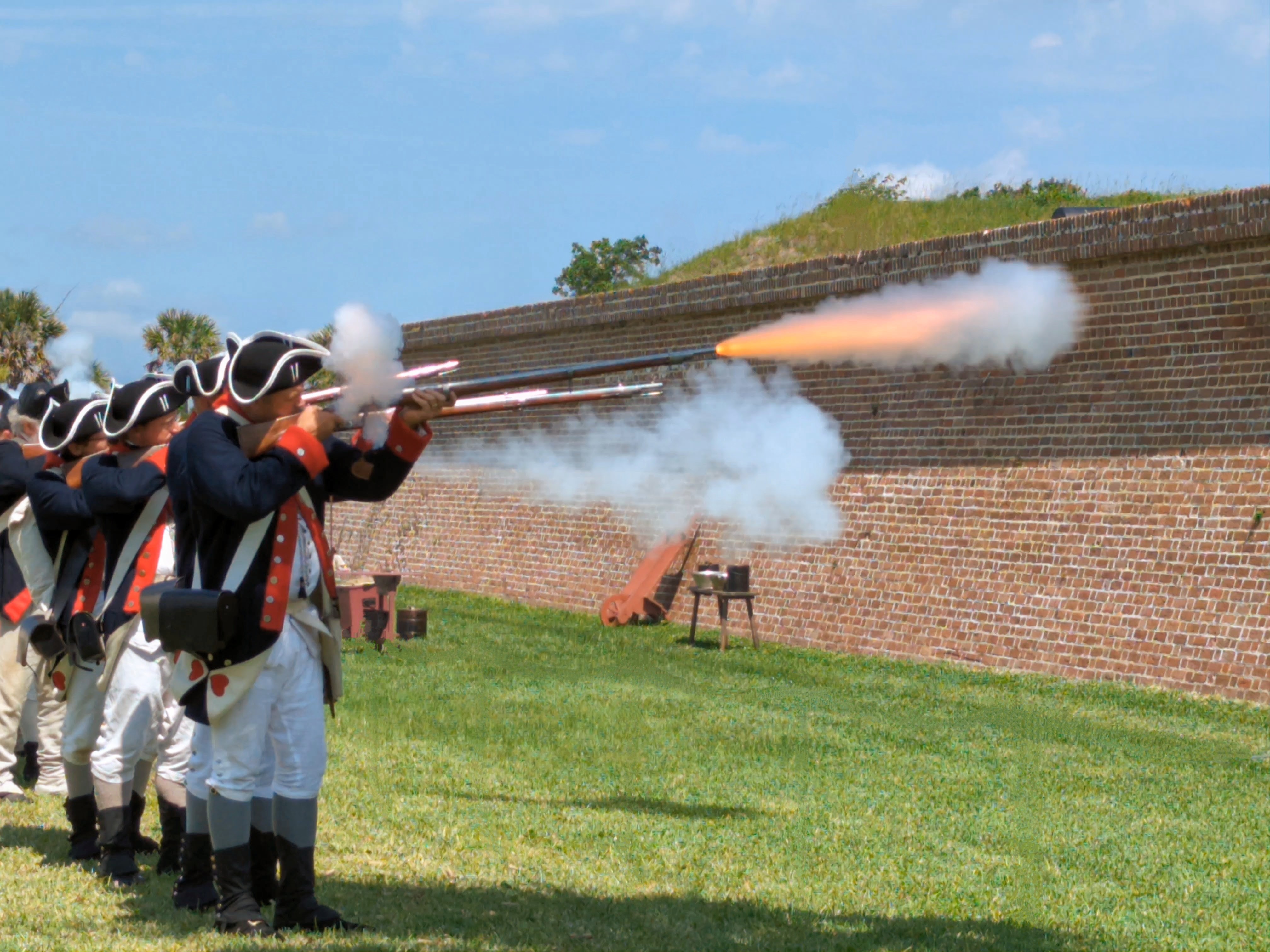 A row of living historians fire muskets during Carolina Day events