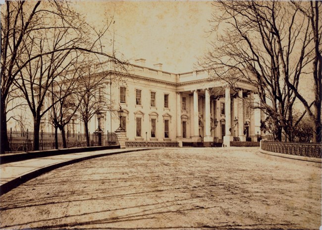 Black and white image of the North portico of the White House with a circular dirt driveway