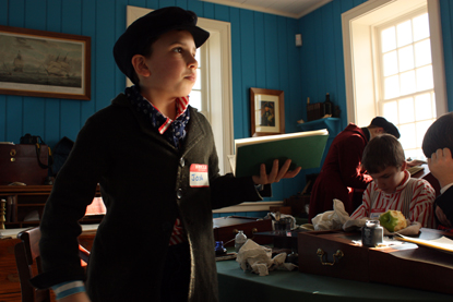 A young boy dresses as a fur trade-era clerk and practices copperplate as part of the Young Engage School.