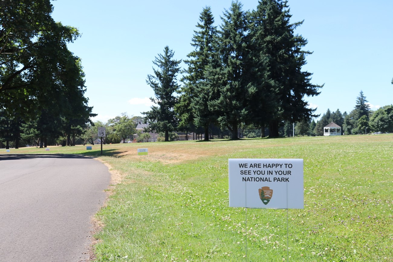 A sign in the grassy area along the park road at Fort Vancouver National Historic Site with the text "We are happy to see you in your national park."