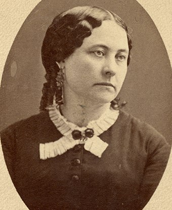 A black and white photo of a middle-aged woman with dark hair wearing a dark dress with a lacey collar.