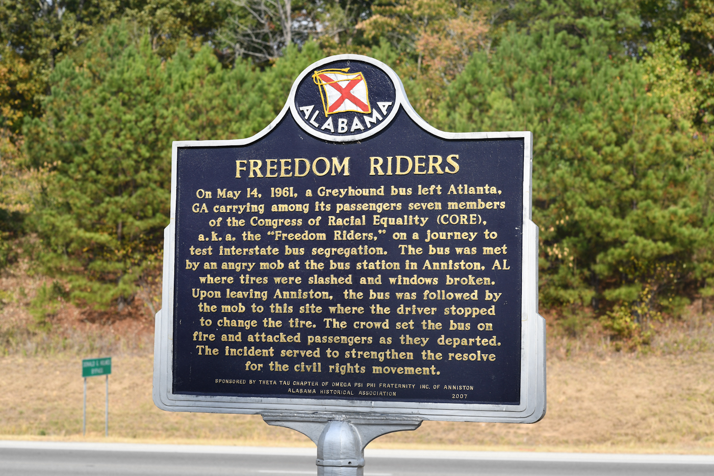 A black metal sign with yellow text tells the story of the freedom riders attacked at this location in 1961.