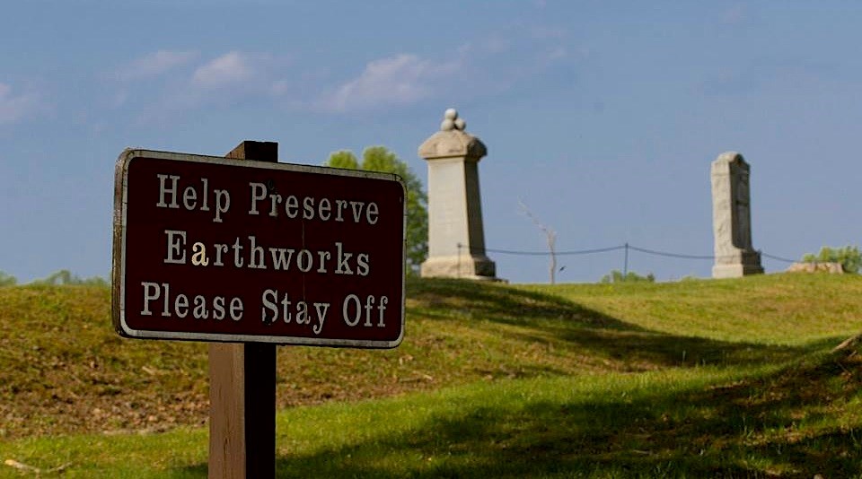 Earthworks at Bloody Angle with two monuments in background and sign reading "Help Preserve Earthworks Please Stay Off" in foreground