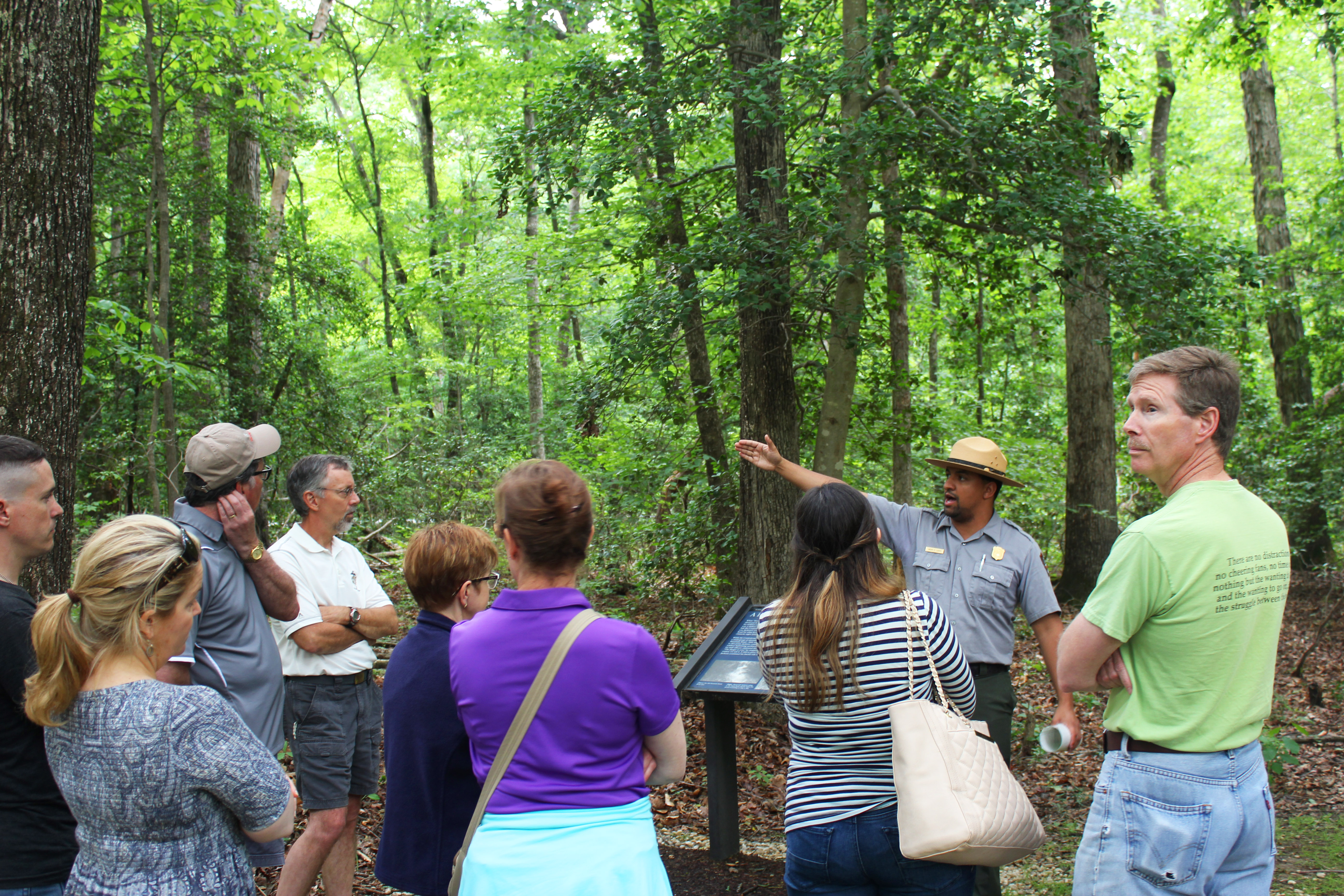 Crowd listens intently as ranger points in the distance with trees in the background