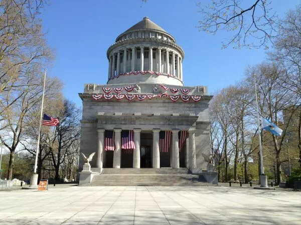 Grant's Tomb decorated with American flags and buntings, and two flags in the foreground are flying at half staff.