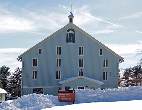 The Eisenhower barn has large piles of snow around it. The park sign is in the foreground.