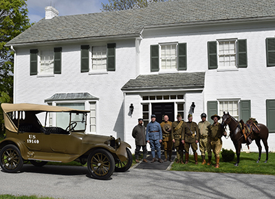 WWI reenactors stand with a horse and a vintage WWI era military vehicle