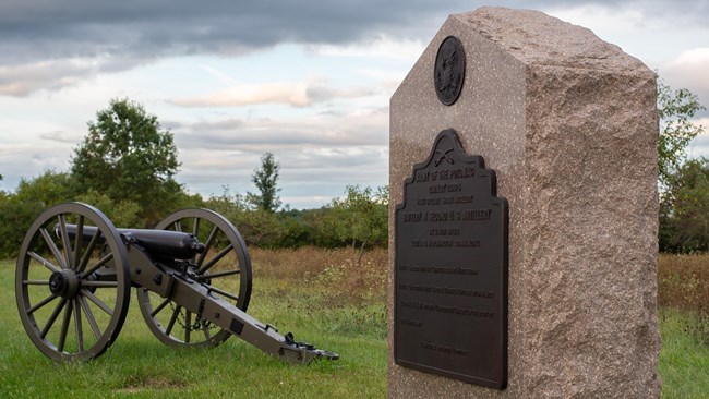 An artillery piece stands next to a stone and bronze monument marker