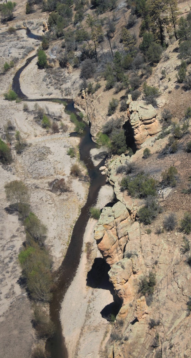 A winding fork of the Gila River meanders through the desert as seen from rocky cliffs above.