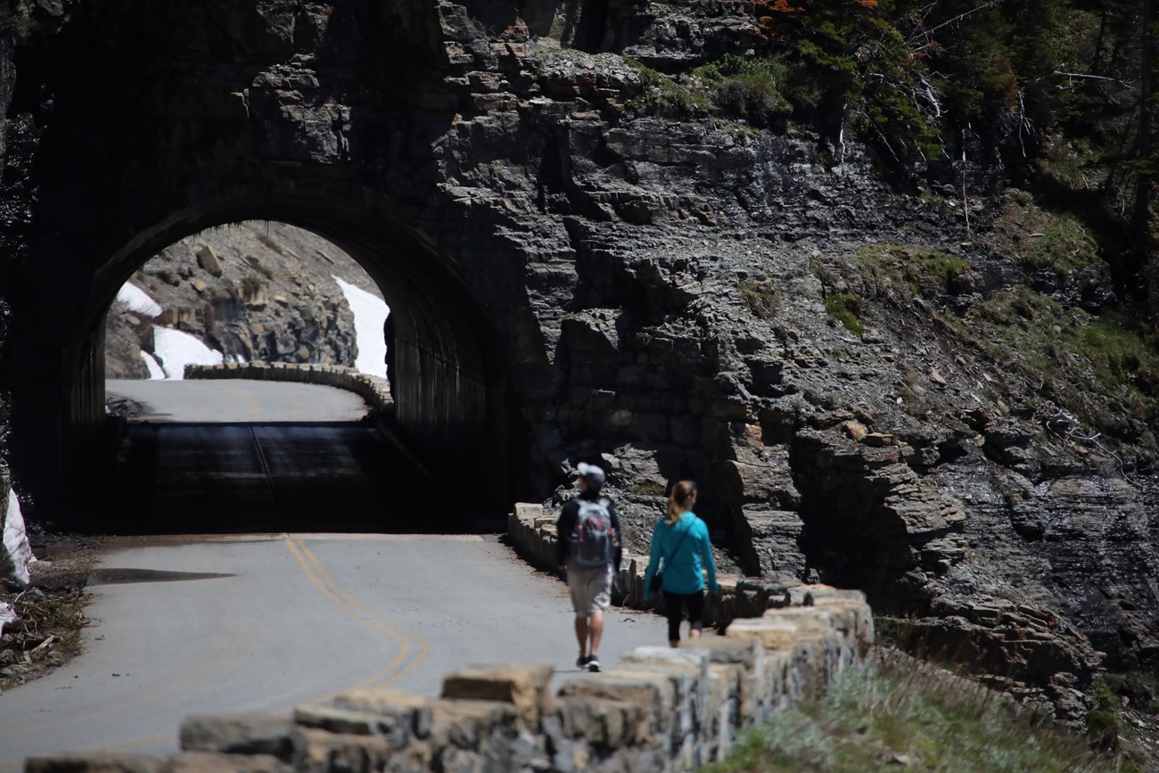 West side tunnel on Going to the Sun Road with two hikers walking towards it going east