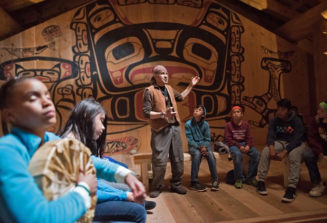 Elder and youth in Tribal House An elder speaks to listening youth inside the Huna Tribal House.