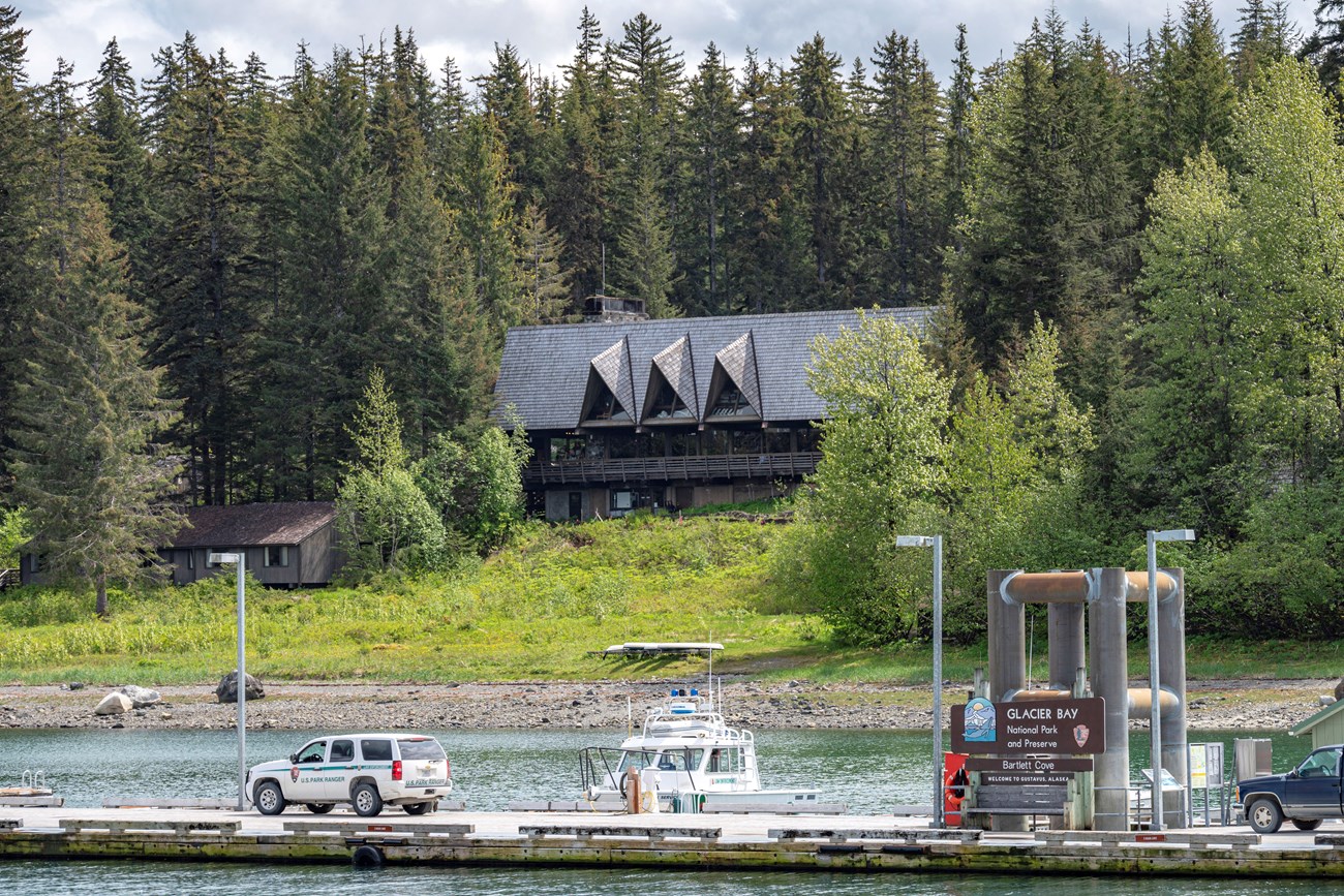 The Glacier Bay Lodge nestled in a dense forest on the shore of Bartlett Cove, the dock is visible in the foreground.