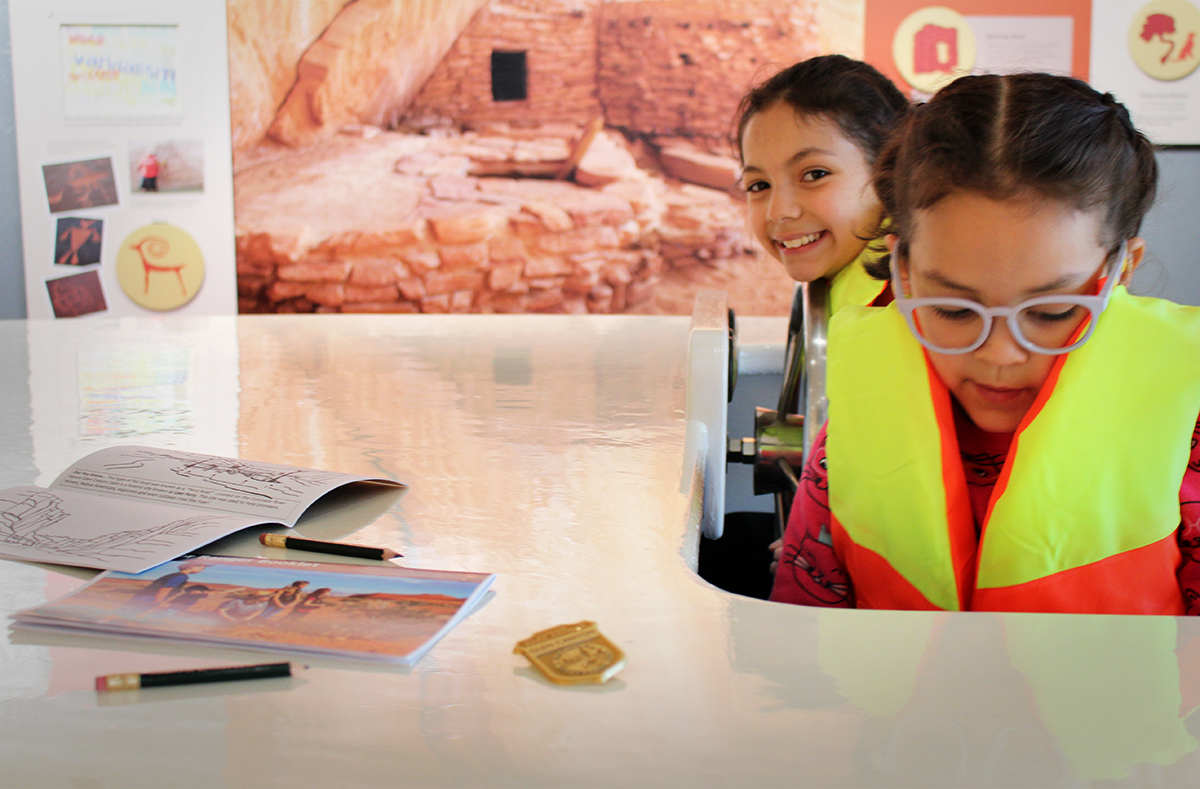 Two girls wearing life jackets in play boat with exhibit panels in background