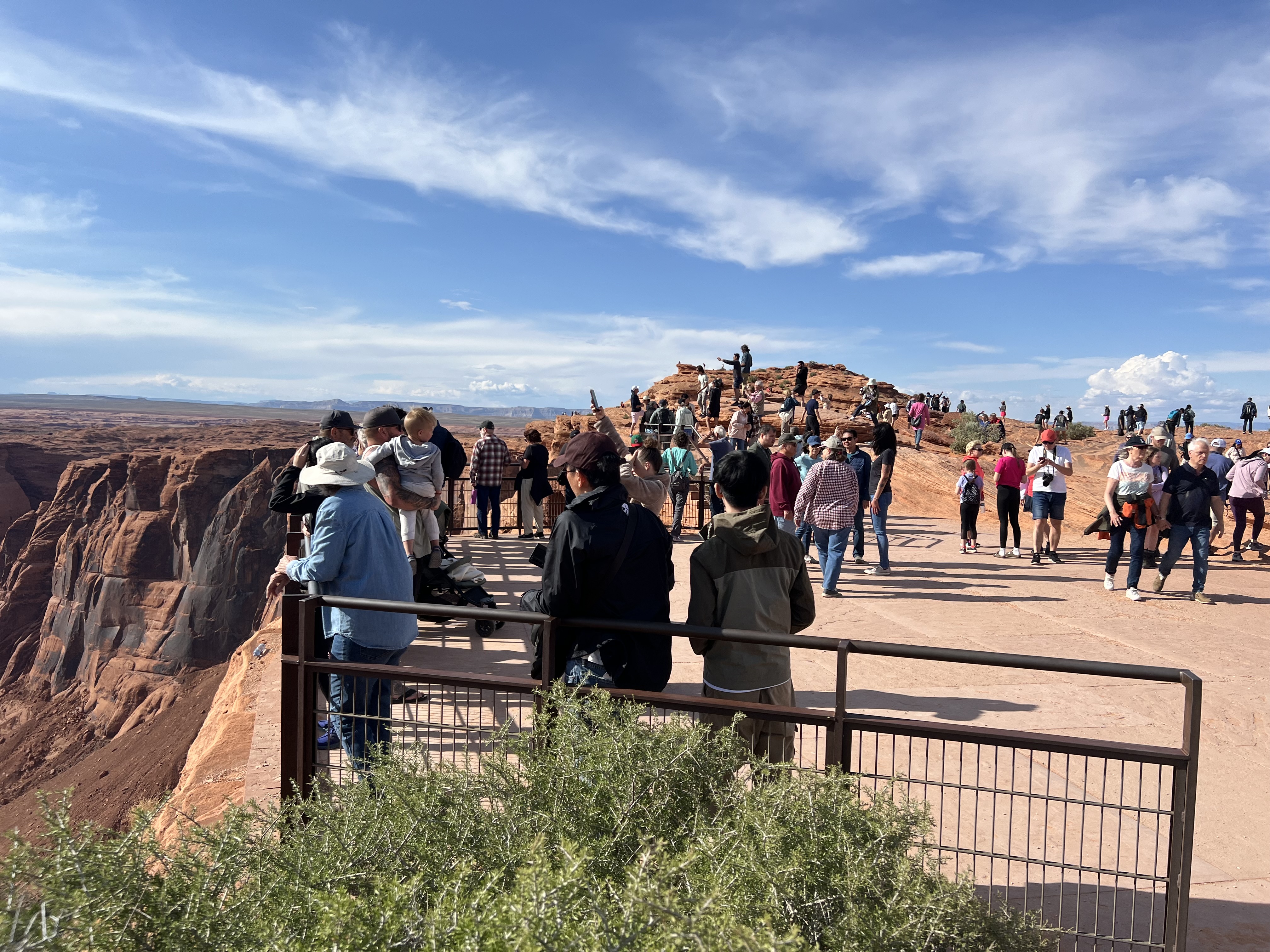 a large group of people standing all over the rocks and surfaces behind a metal railing at a cliff.