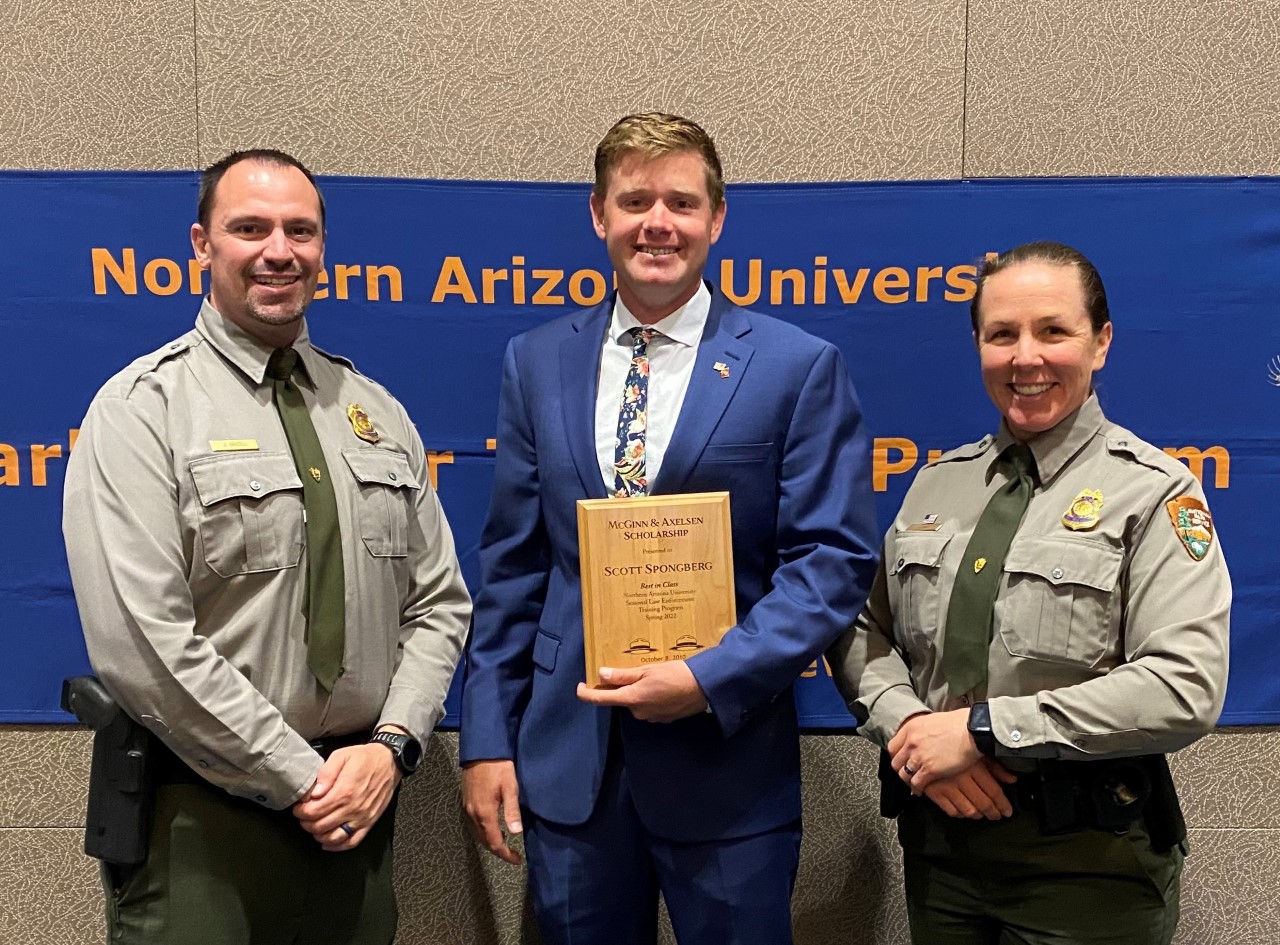 three people stand next to each other posing for a picture smiling , the middle person holding award plaque