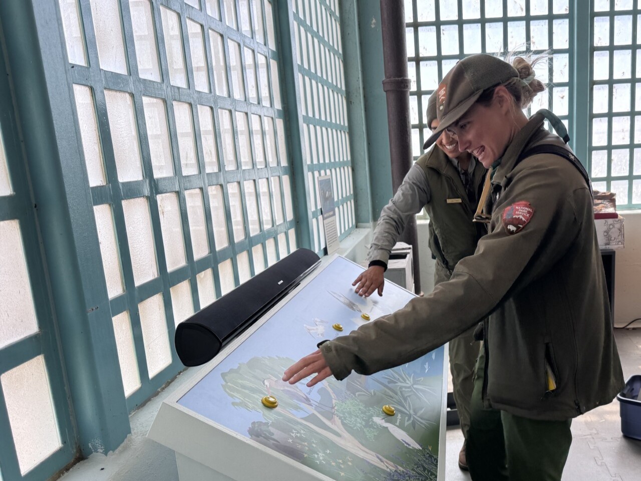 Two NPS staff members stand next to an interpretive display, pointing at its buttons