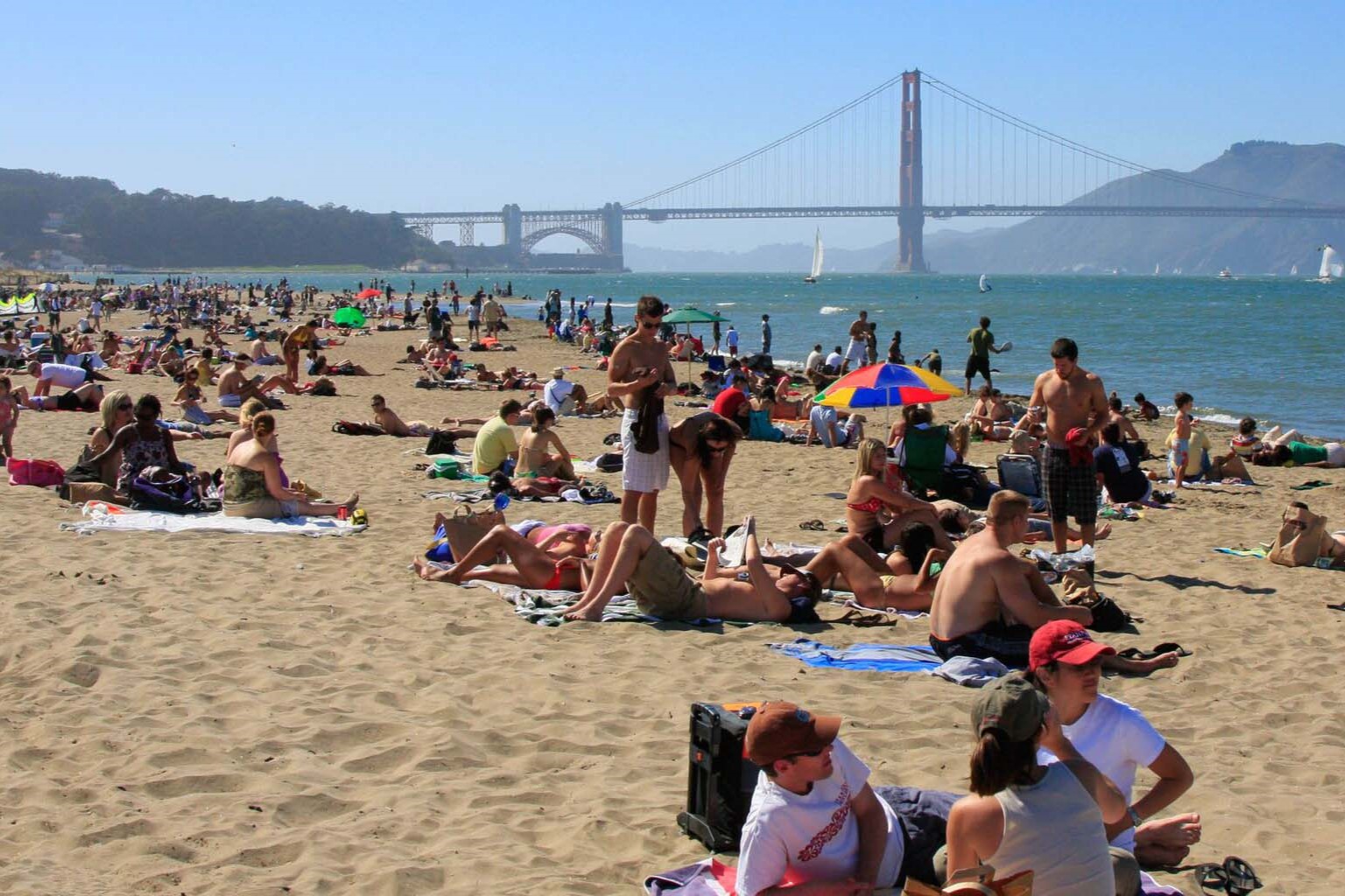 A large group of people at a beach with the Golden Gate Bridge in the distance