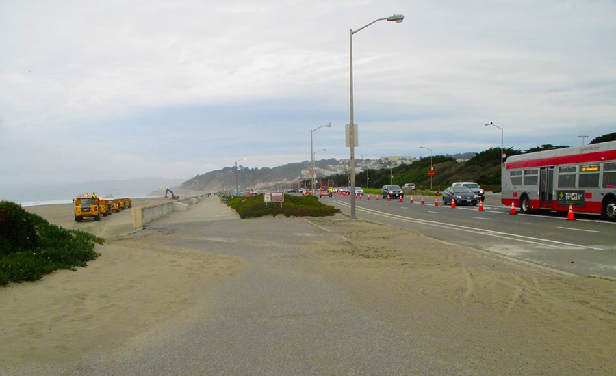 trucks carrying sand travel down Ocean Beach