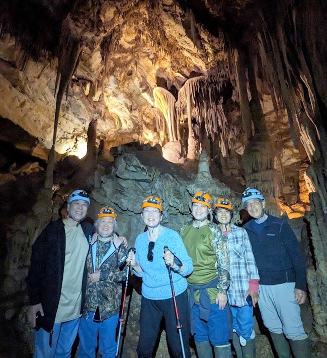 Six people standing in cave with helmets on below the parachute shield in Lehman Caves