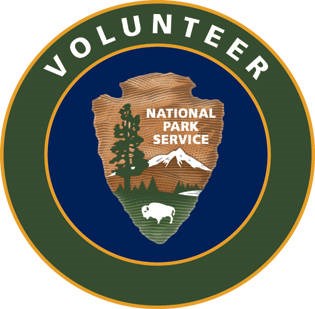 National Park Service Volunteer patch is circular with the words "volunteer" in white letters against a green outer circle. An inner circle is navy blue and has an NPS arrowhead graphic with a bison, a tall tree, and a snow-covered mountain positioned wit
